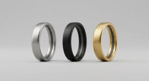 Three slim titanium smart rings in silver, black and gold standing in a row on a light gray studio backdrop, no readable text or logos